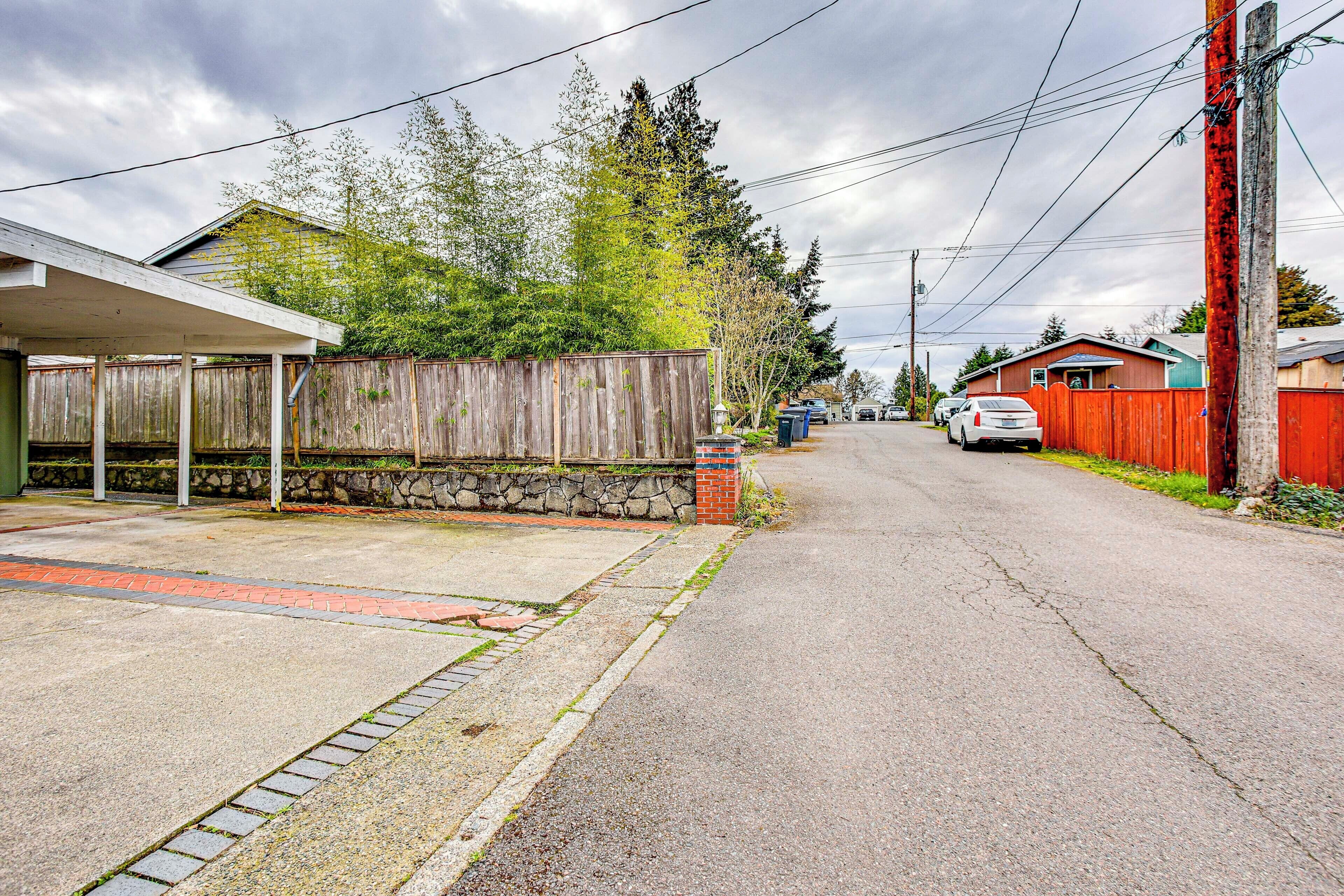 A residential street with houses, a covered parking area, and a wooden fence.