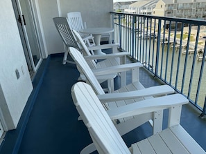 A balcony with white Adirondack chairs and a small round table, overlooking a canal with boats. - Marlin Cove - 2 BR, Sleeps 6, Pool - 120th Bayside (Ocean City)