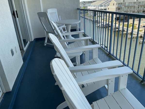 Varanda com cadeiras Adirondack brancas e uma pequena mesa redonda, com vista para um canal e barcos.