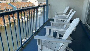 A balcony with white Adirondack chairs, a blue floor, and a view of a marina with boats and buildings in the background.