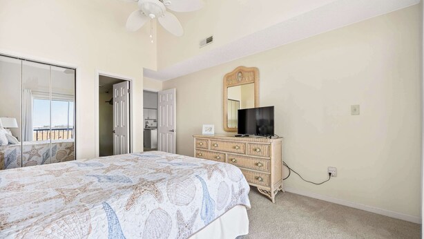 A bedroom with a bed, dresser, television, and a ceiling fan.