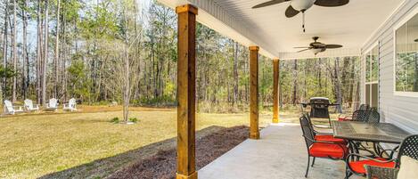A covered patio with a dining table and chairs, a ceiling fan, and a view of a forested area.