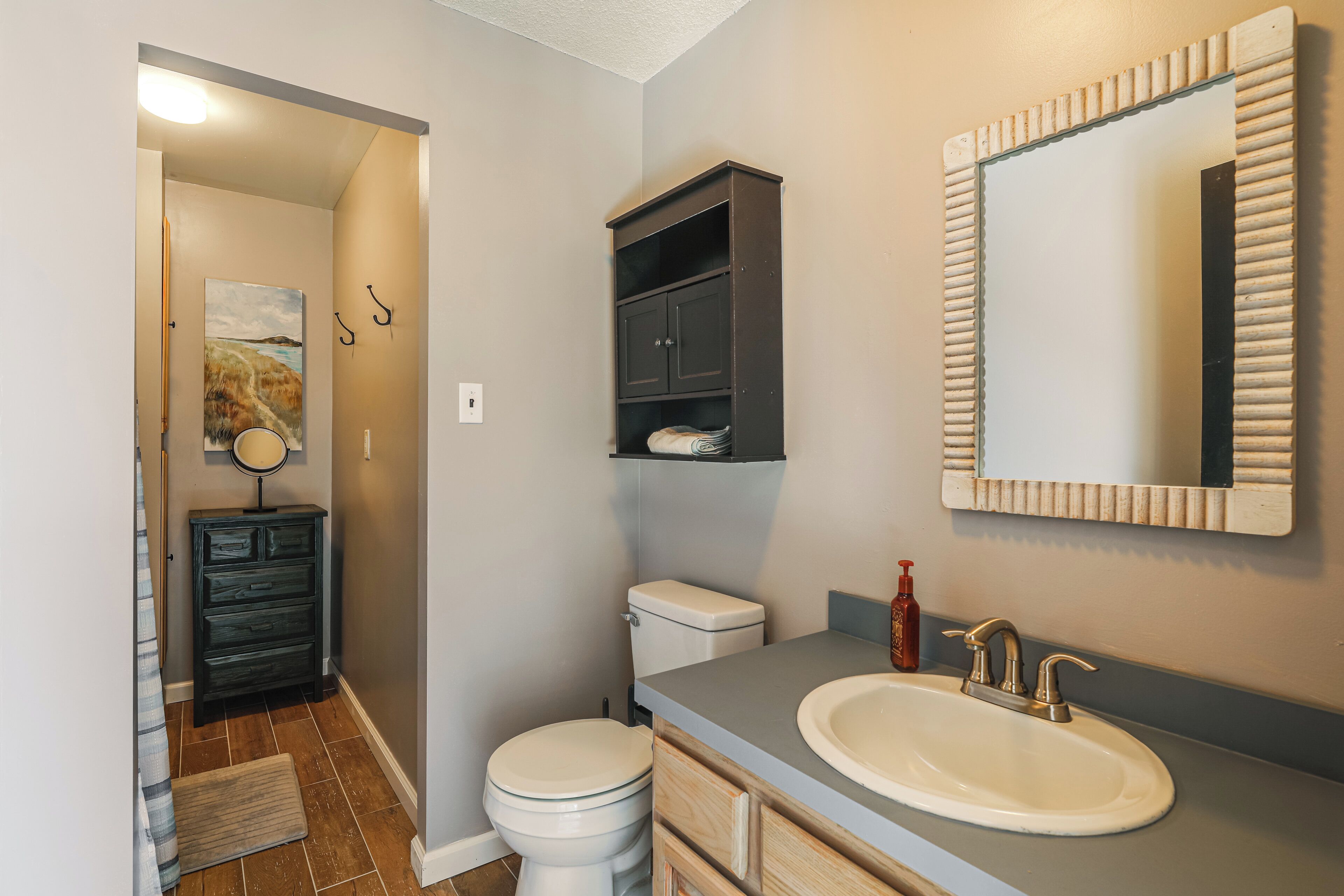 A bathroom with a toilet, a sink with a mirror, a cabinet, and a rug on the floor.