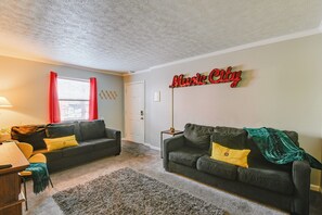 Una sala de estar con dos sofás oscuros, una mesa de madera, una lámpara y un letrero que dice 'Music City' en la pared.