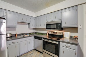 Una cocina con armarios grises, electrodomésticos de acero inoxidable y piso de baldosas de piedra.