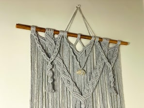 A macramé wall hanging with a wooden rod and tassels. - Pousada Quartzo (Alto Paraíso de Goiás)