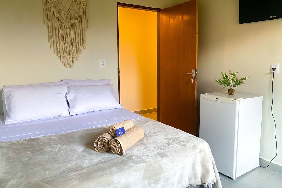 Une chambre d’hôtel avec un lit, une porte en bois, un petit réfrigérateur blanc et un téléviseur fixé au mur.