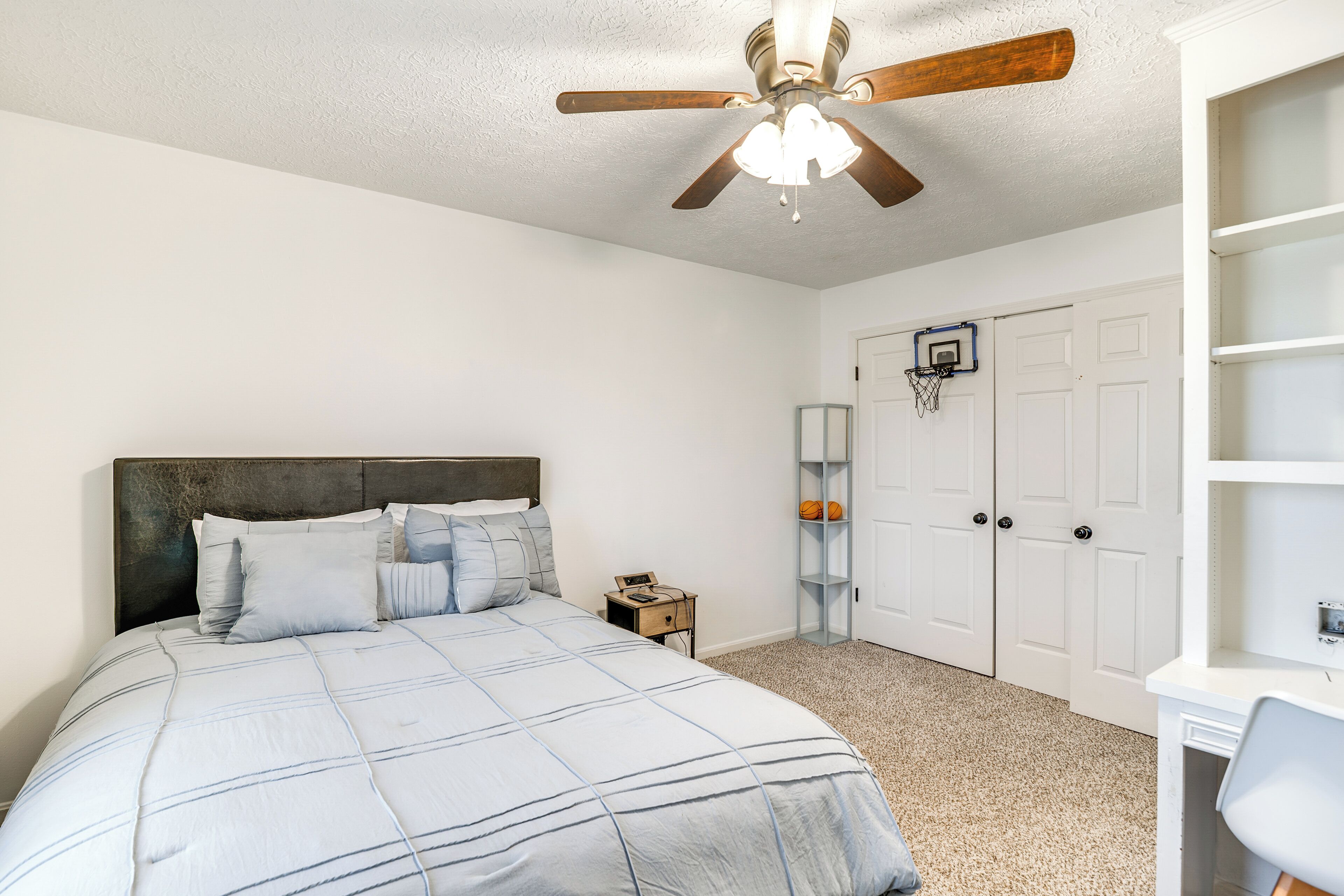 A bedroom with a bed, a ceiling fan, a basketball hoop, and a white door.