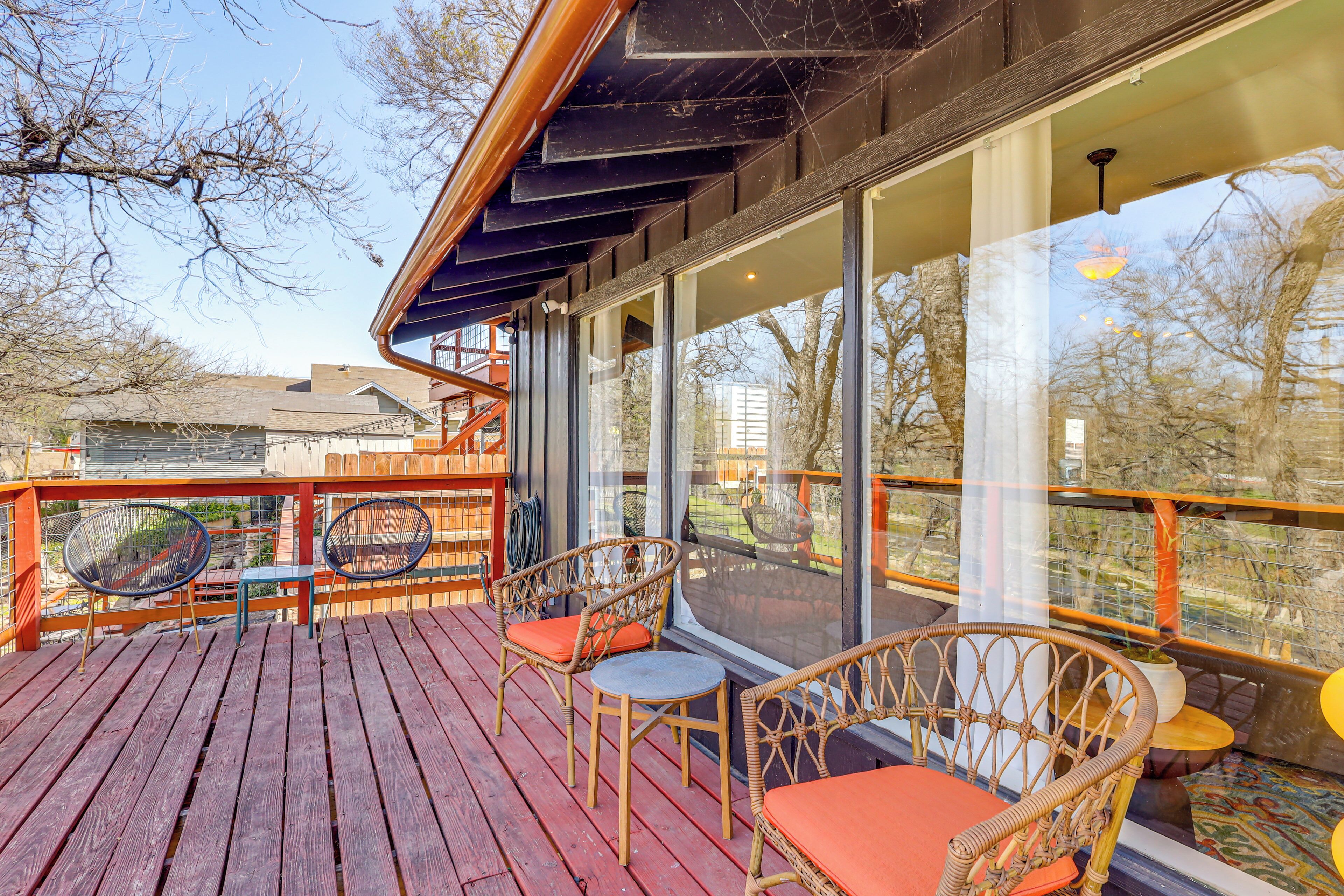 A wooden deck with wicker furniture and a glass railing overlooking a residential area.