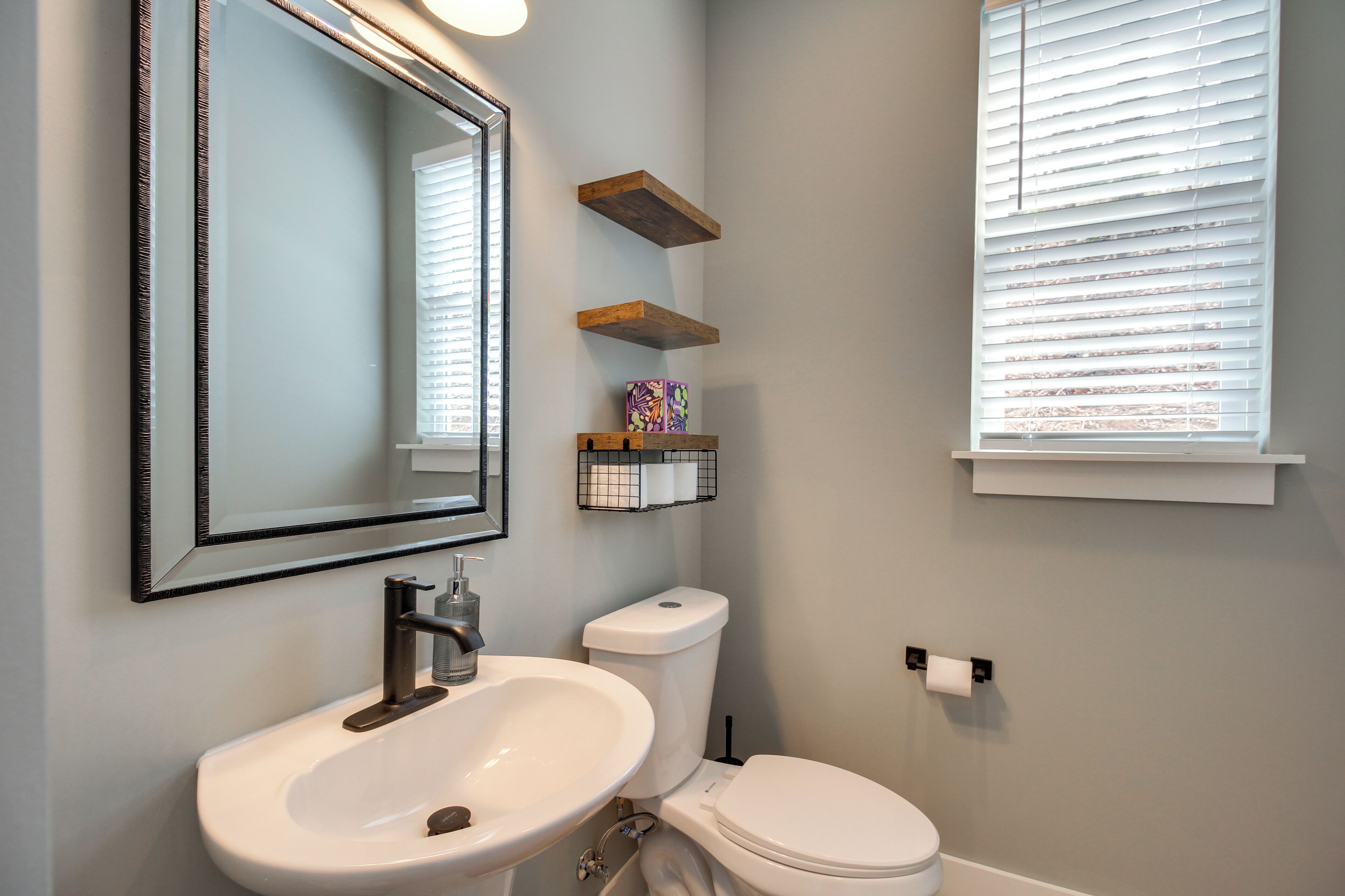 A bathroom with a sink, toilet, and window with blinds.