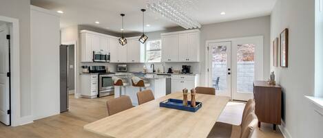 A modern kitchen with white cabinets, stainless steel appliances, and a dining area with a wooden table and chairs.