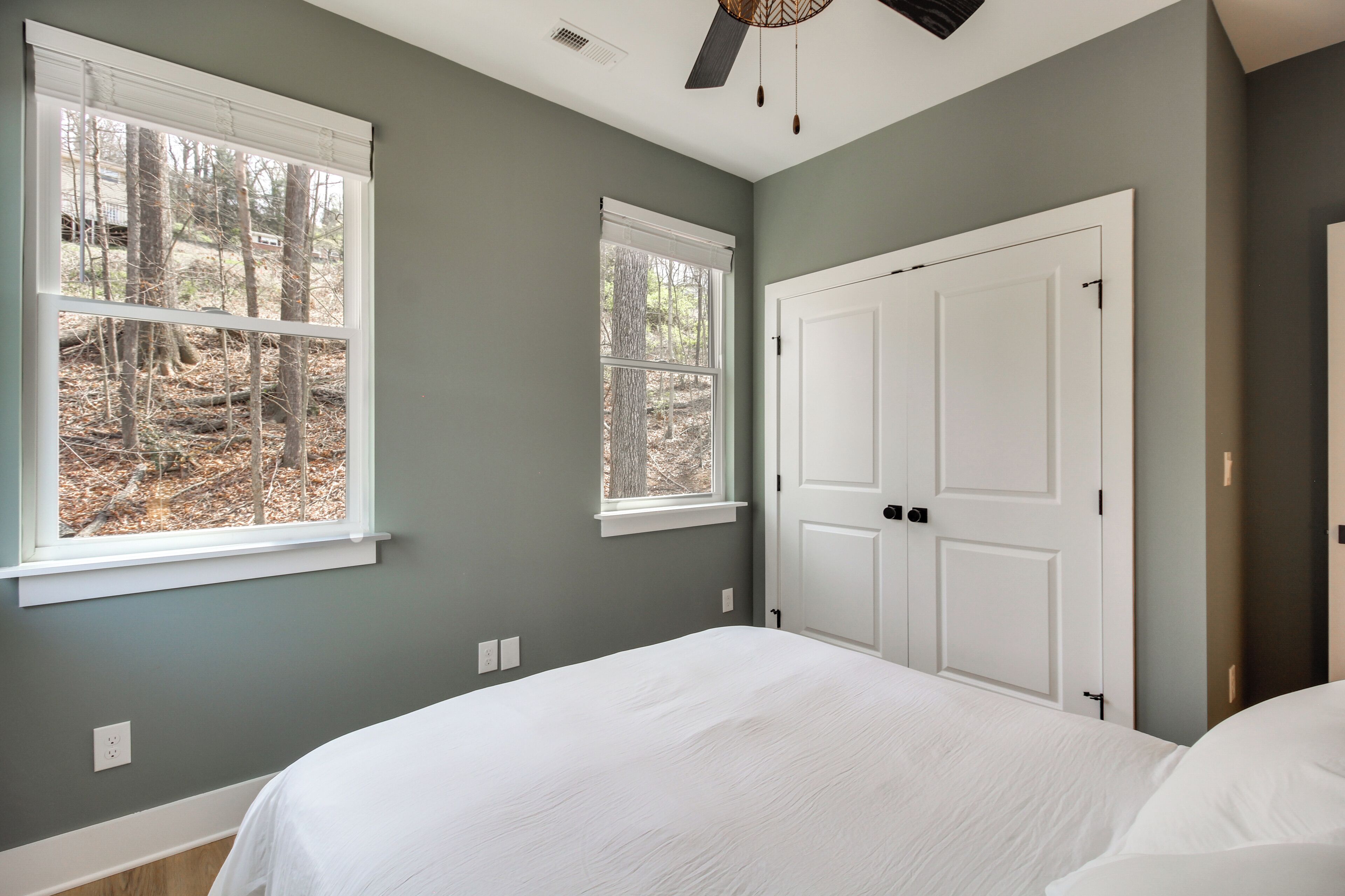 A bedroom with two windows, a bed, and a door.
