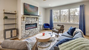 A living room with a stone fireplace, a ceiling fan, a large window with curtains, and a cozy seating area. - 6 Mi to Chattanooga: Home w/ Balcony & Dtwn Views! (Rossville)