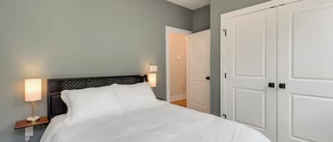 A neatly made bed with white linens, a nightstand with a lamp, and a closed door in a room with light blue walls.