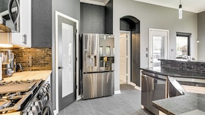 A modern kitchen with stainless steel appliances, a brick backsplash, and a dark gray wall. - Private Pool & Hot Tub: 'wild Horse' Home! (College Station)