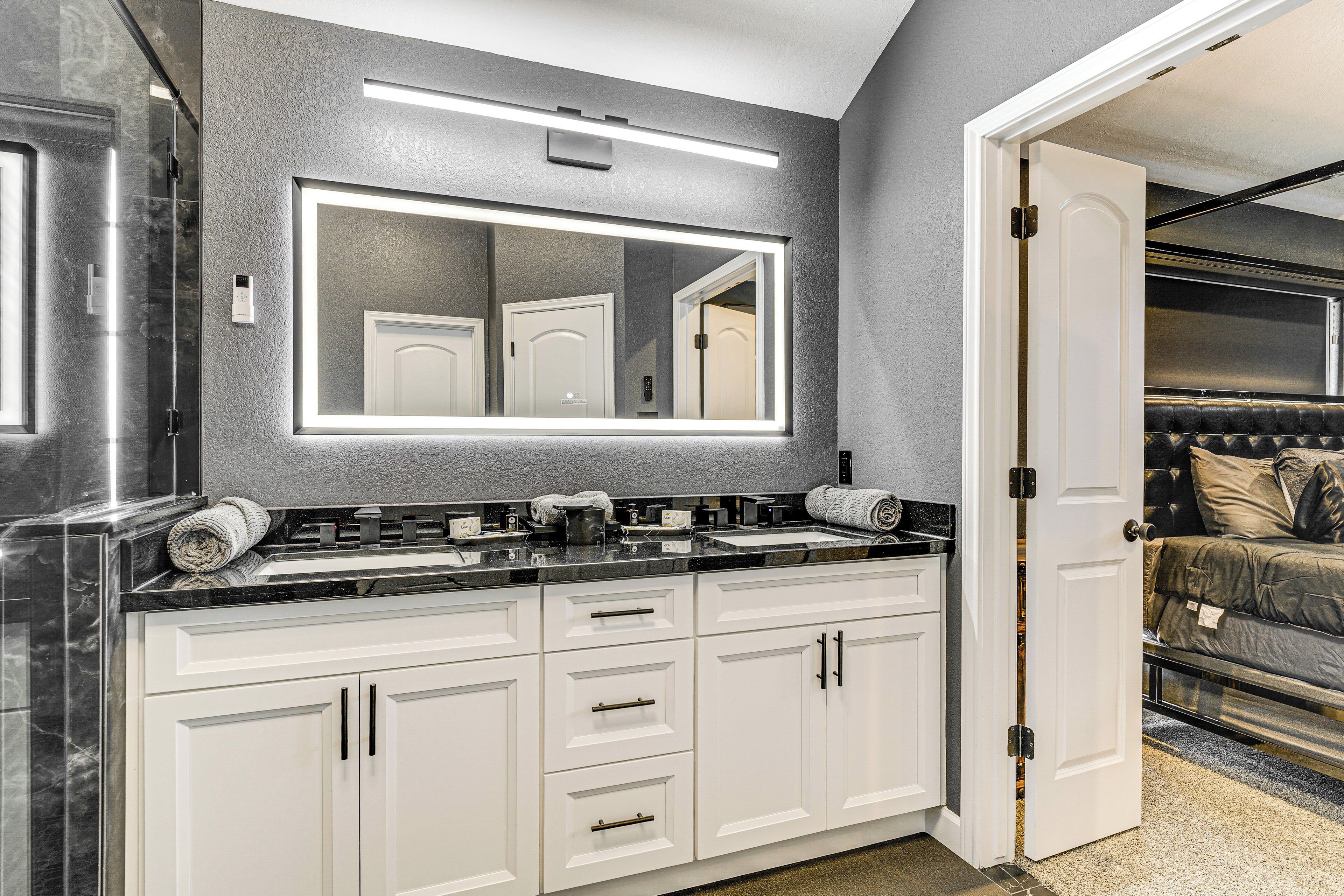 Un baño moderno con un espejo grande, muebles blancos y una zona de ducha.
