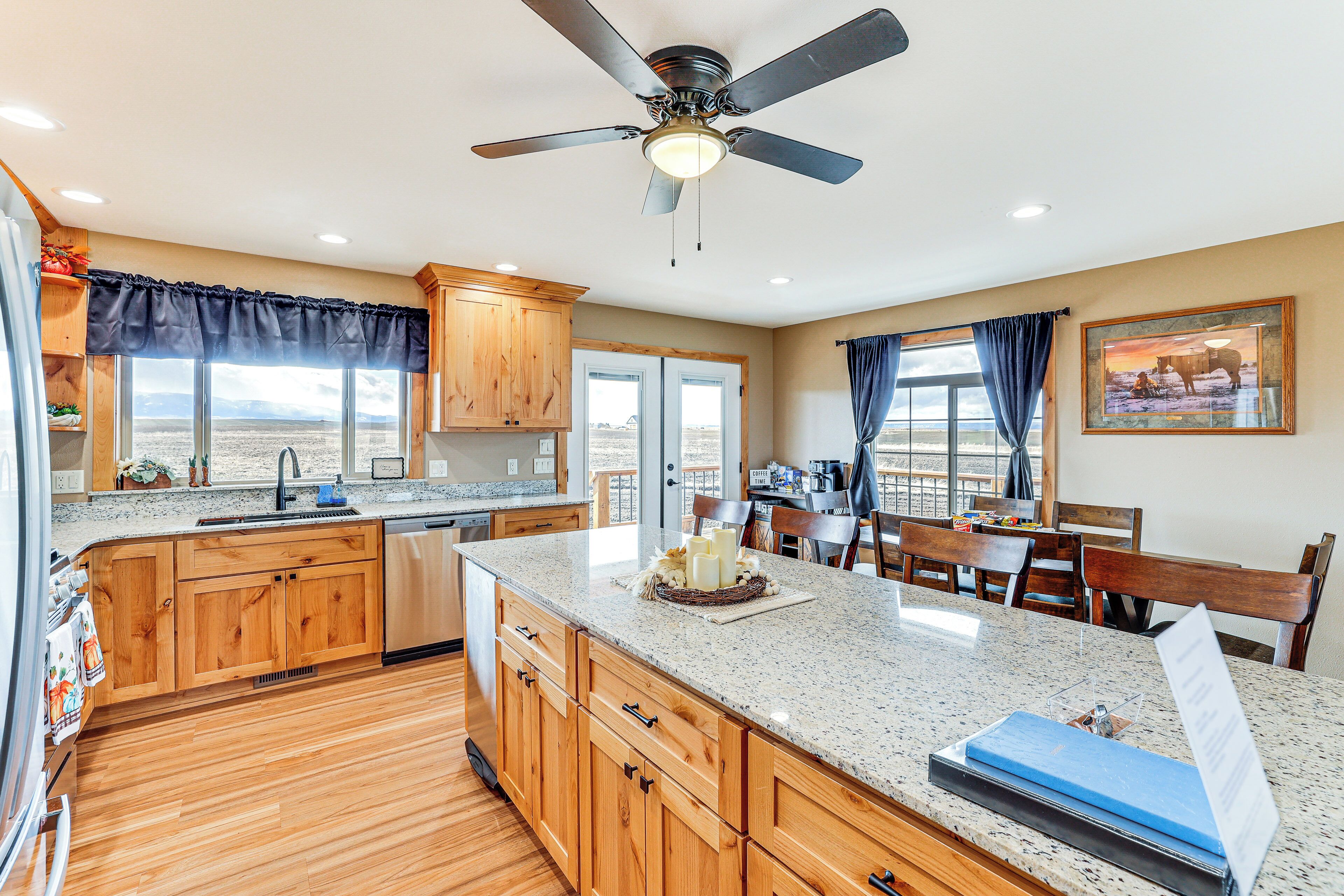 A kitchen with wooden cabinets, a granite countertop, a ceiling fan, and a view of the desert through large windows.