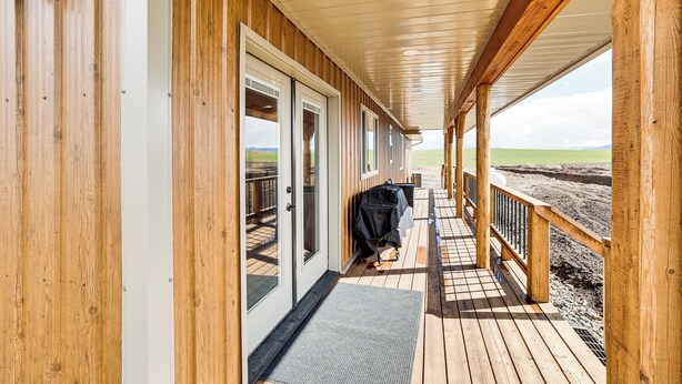 Una terraza de madera con una zona cubierta, barandillas de madera y vistas al paisaje.