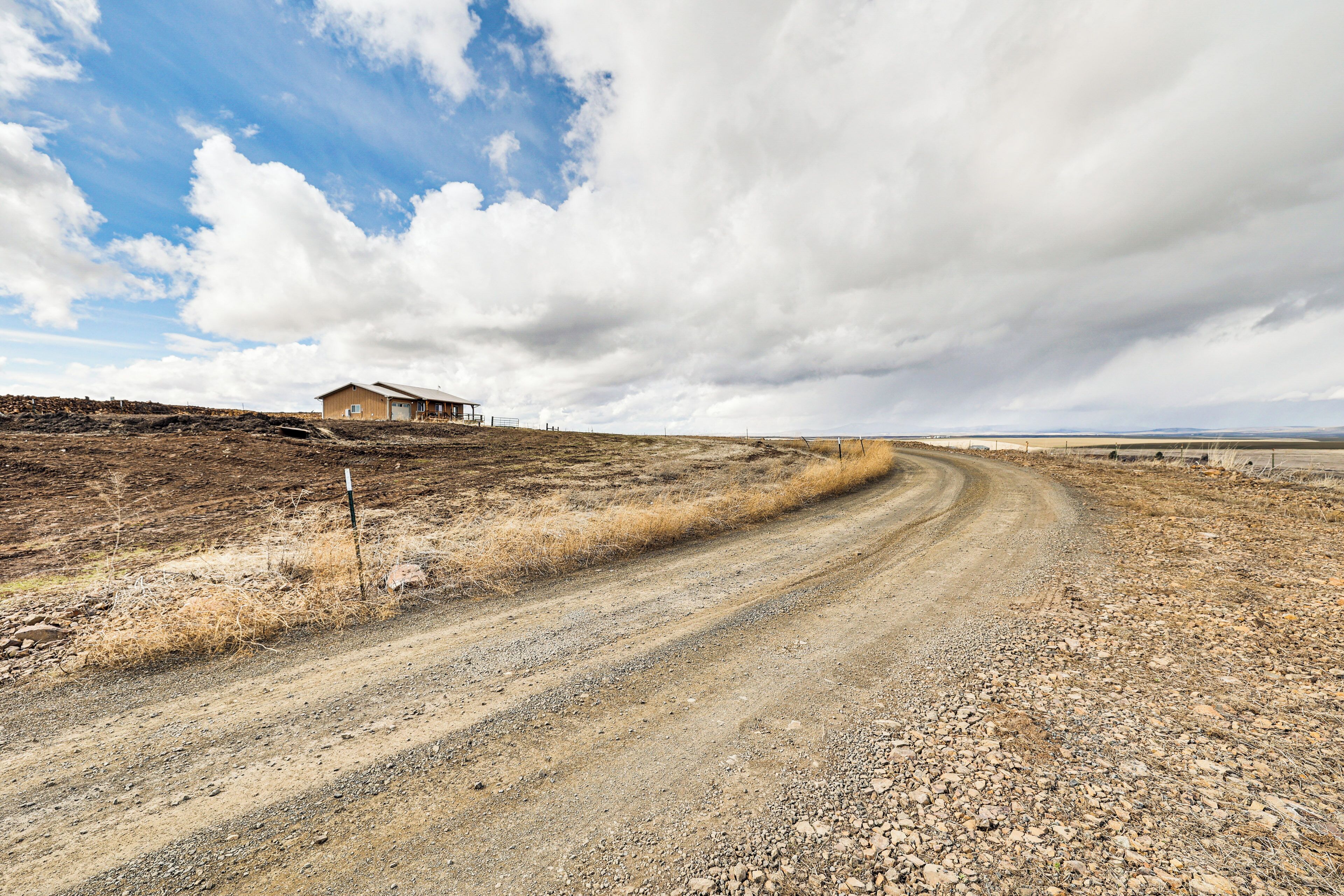 A rural road leading to a small building with a dirt path and sparse vegetation.