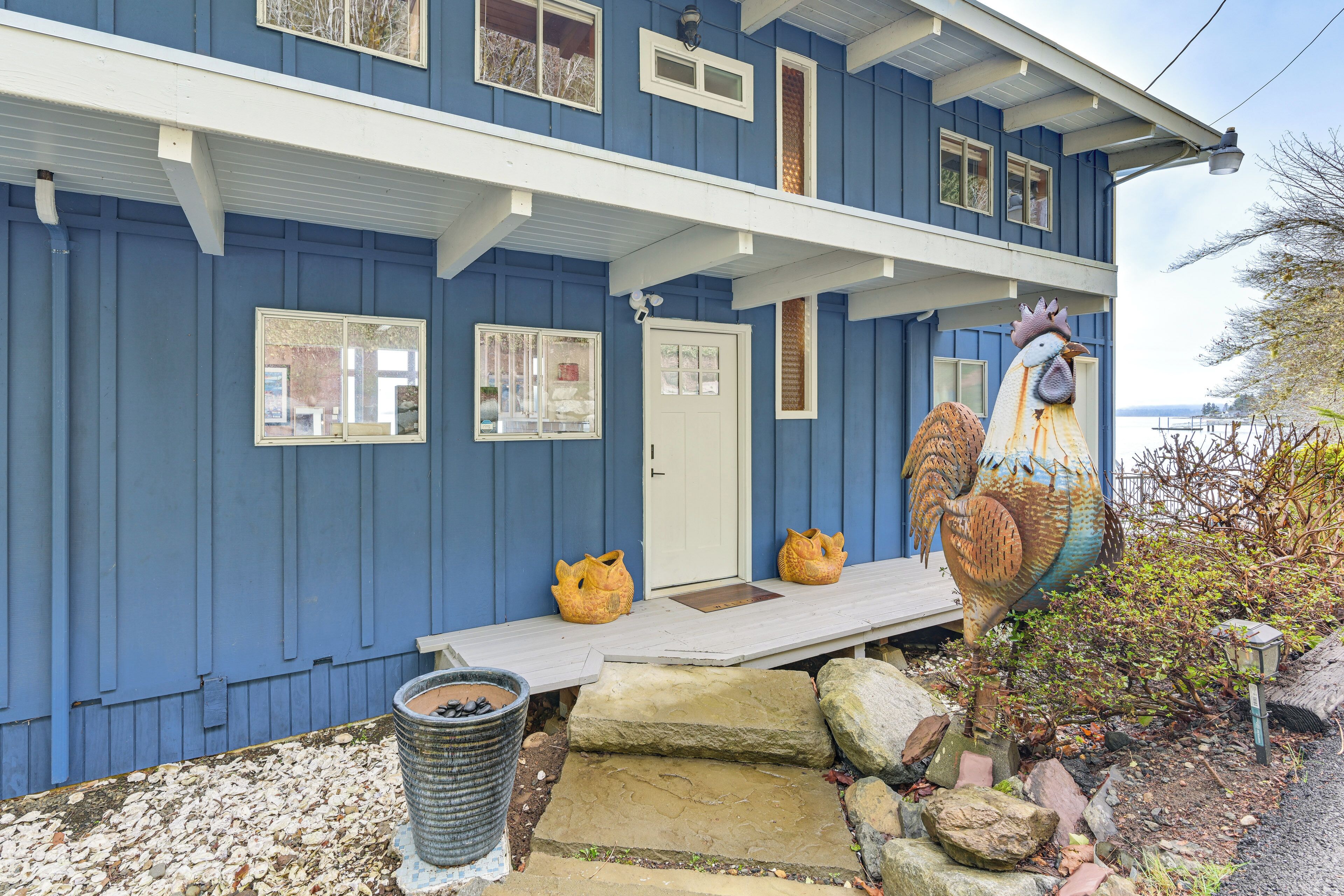 Una casa de dos pisos con fachada azul, un porche delantero y una gran escultura de gallo.