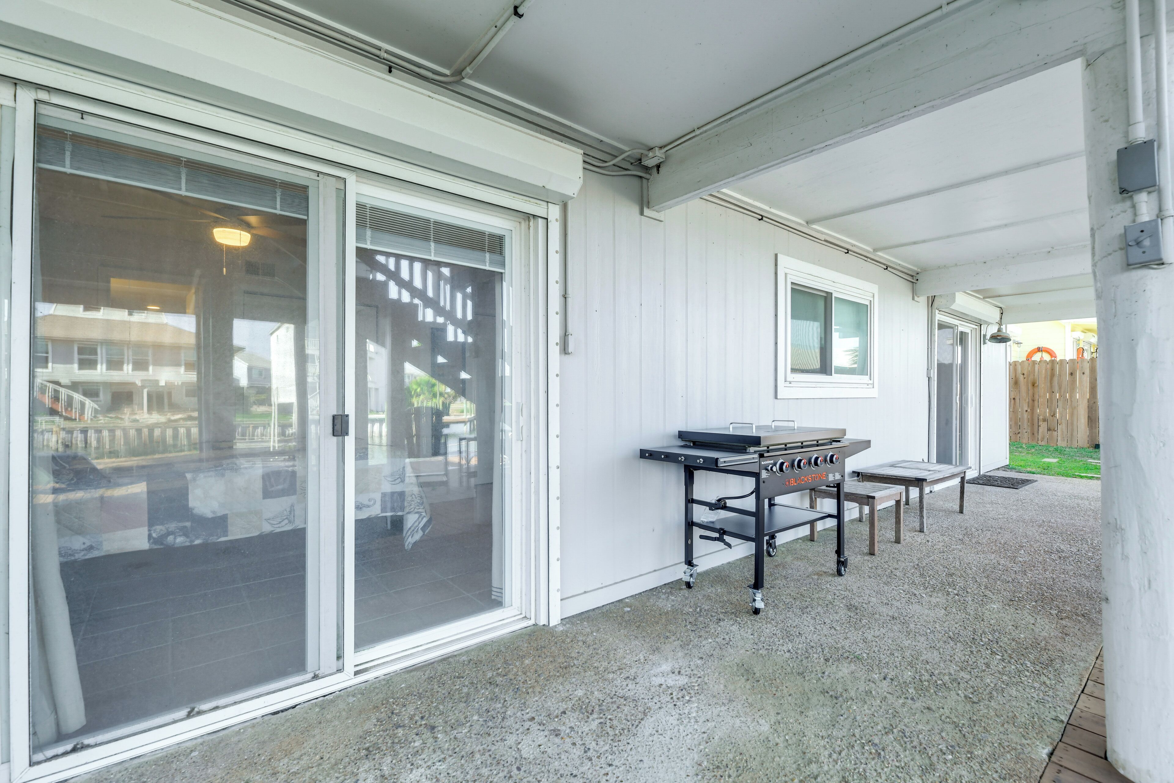 A covered patio area with a grill and tables, large sliding glass doors, and a view of a backyard.