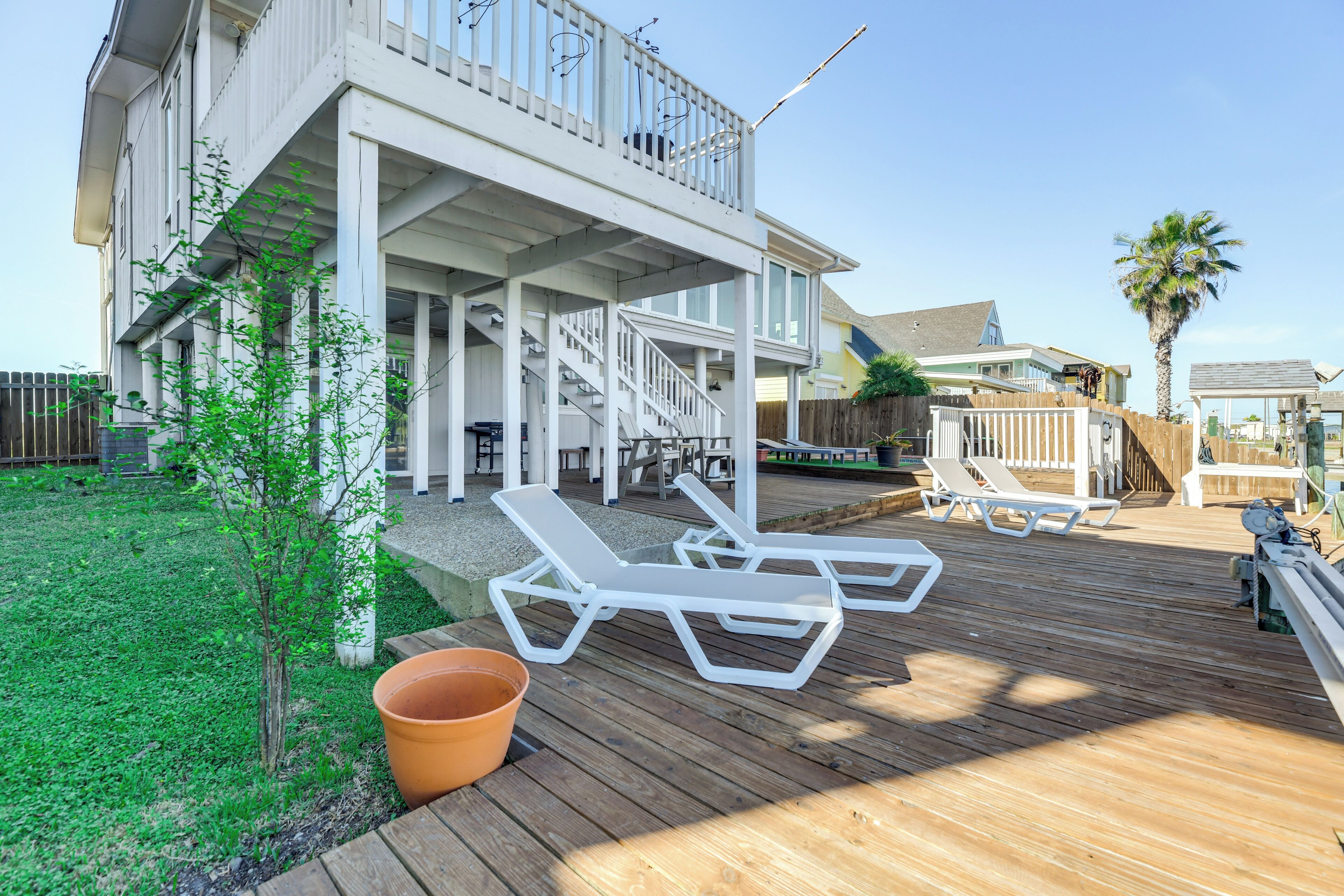 A wooden deck with white lounge chairs, a small tree, and a terracotta pot.