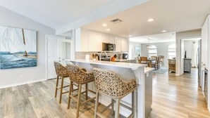 Une cuisine moderne avec des meubles blancs, un îlot central doté de tabourets et un grand tableau accroché au mur.