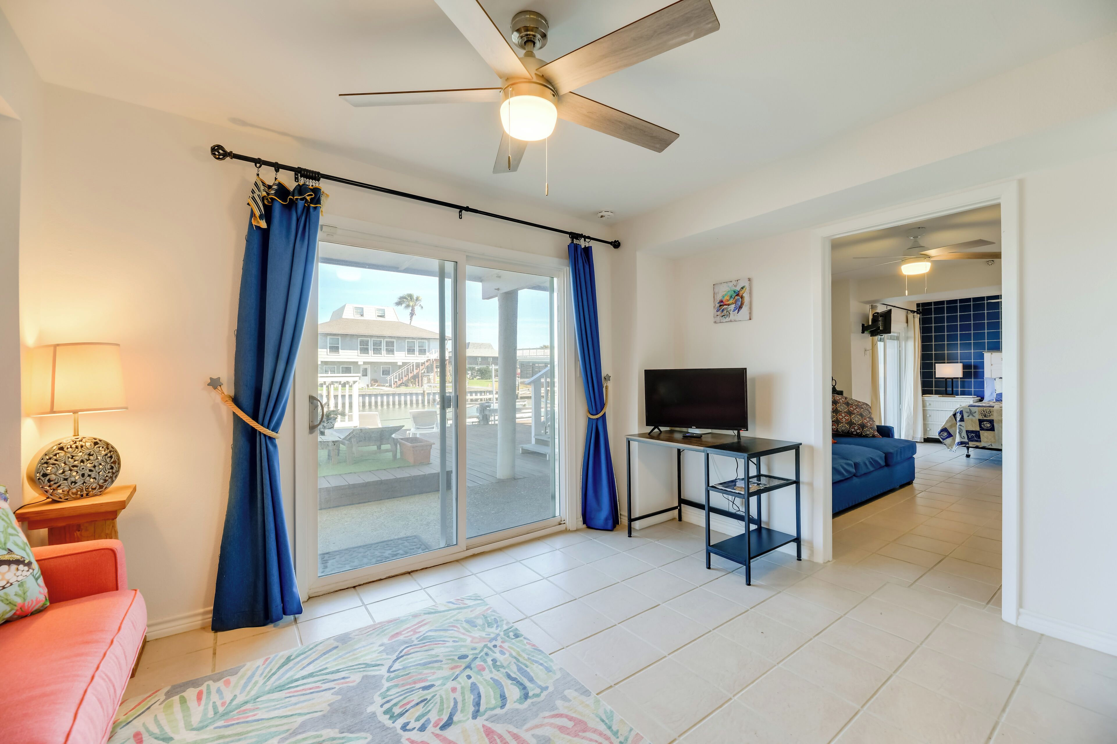 A living room with a TV, a ceiling fan, and a view of a balcony.