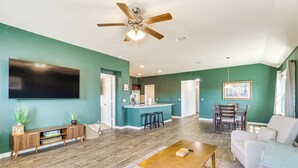 A spacious living room with a wooden floor, a ceiling fan, a flat-screen TV, a dining area with a table and chairs, and a kitchen area with a bar counter. - Shop, Dine & Unwind: Pet-friendly Home in Austin! (Austin)