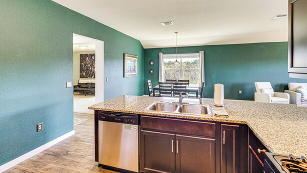 A kitchen with dark wood cabinets, a stainless steel dishwasher, and a granite countertop. - Shop, Dine & Unwind: Pet-friendly Home in Austin! (Austin)