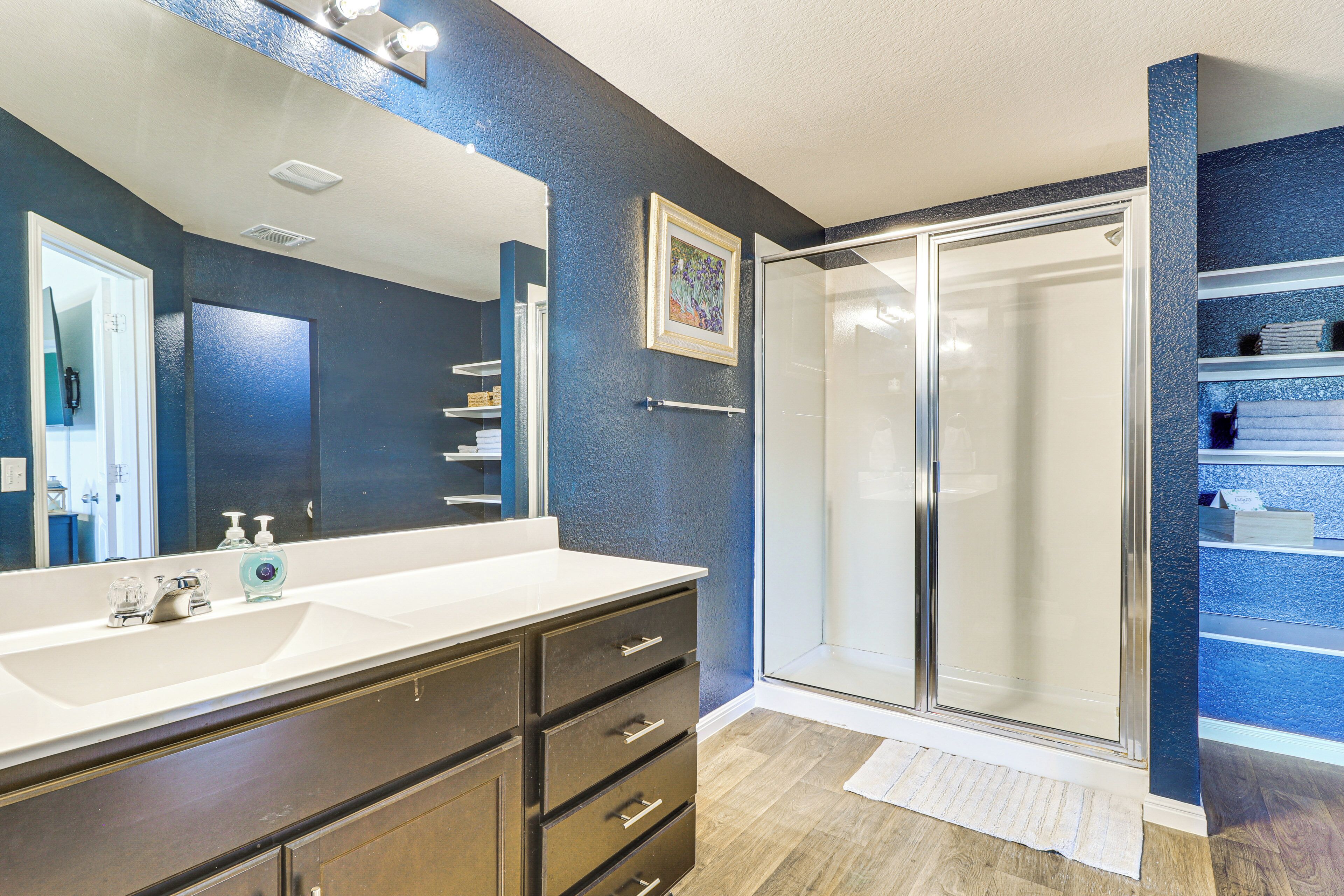 A bathroom with a large mirror, a white sink, a dark wooden vanity, and a glass shower enclosure.