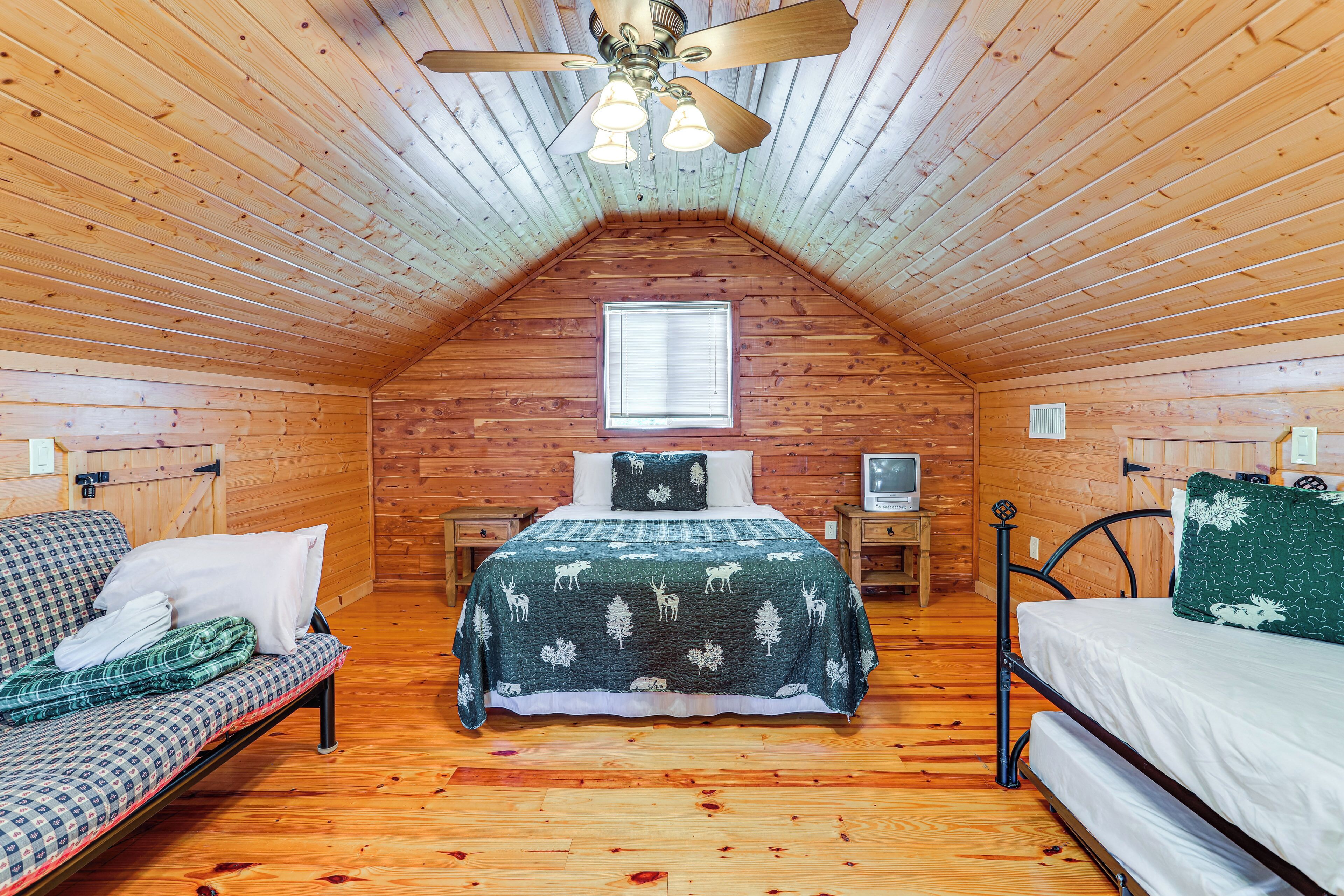 A cozy attic bedroom with a sloped ceiling, a bed with a forest-themed bedspread, a sofa with a checkered cover, and a small window.