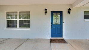 A house with a blue door, two windows with blinds, and two wall-mounted lanterns. - Stay & Play in Belleview: Welcoming Home w/ Yard (Belleview)
