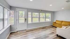 A room with a door, large windows, a wooden floor, and a yellow sofa. - Stay & Play in Belleview: Welcoming Home w/ Yard (Belleview)