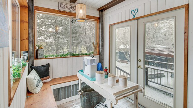 Un acogedor interior de cabaña con un banco de madera, una cafetera y una ventana con vistas a árboles nevados.