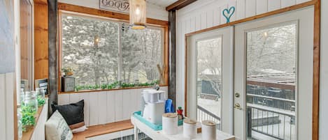 Un acogedor interior de cabaña con un banco de madera, una cafetera y una ventana con vistas a árboles nevados.