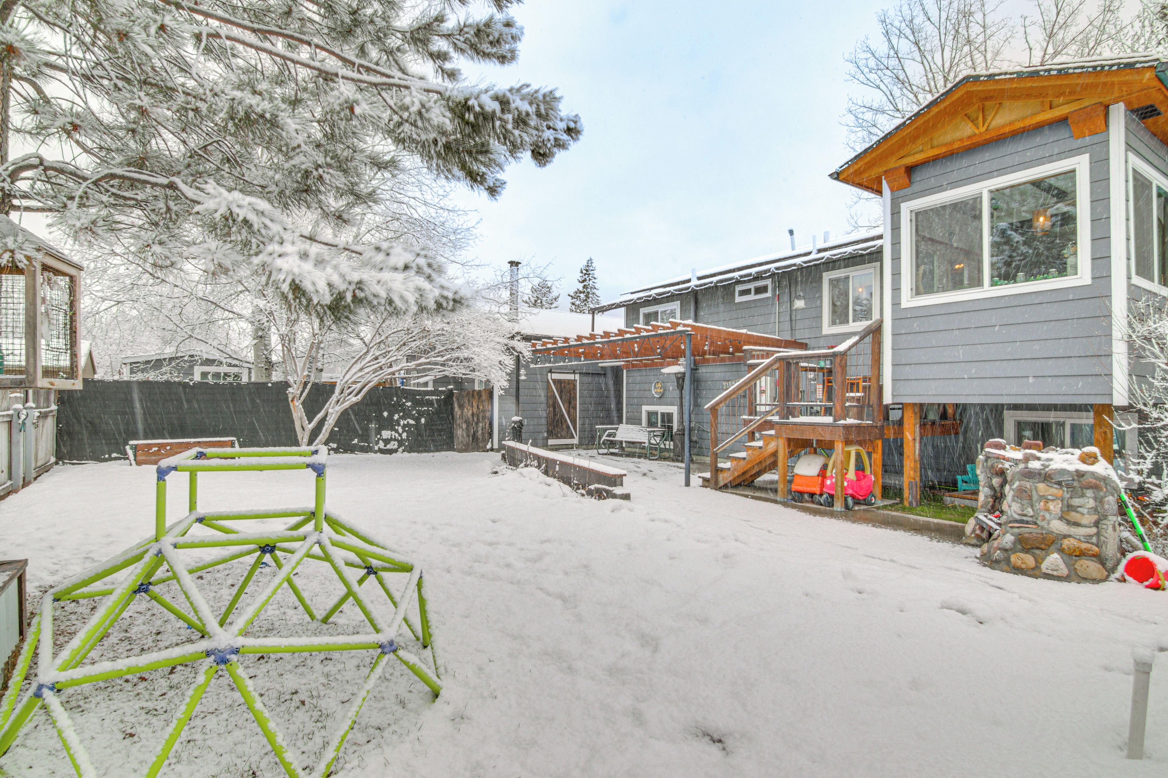 A residential area with a wooden deck, a stone wall, and a metal play structure in the snow.
