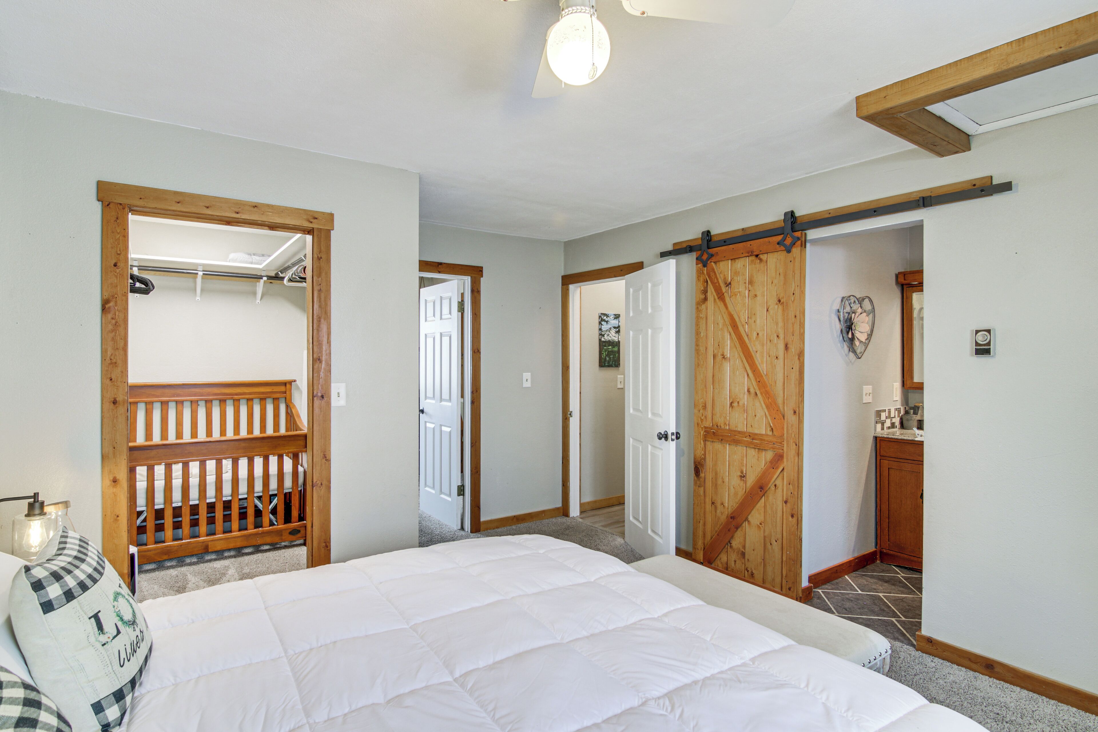 A bedroom with a large bed, wooden door, and a small kitchen area visible through an open door.