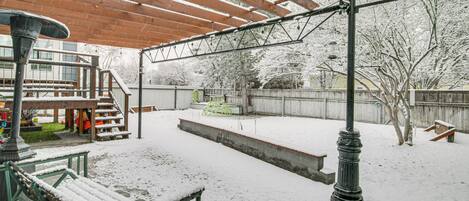 Un espace extérieur abrité, doté d’une pergola en bois, d’un banc et d’un lampadaire.