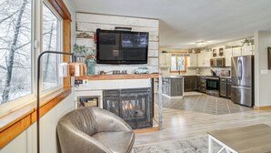 Una cocina moderna con estufa integrada, un televisor grande y una zona de comedor con mesa y sillas.