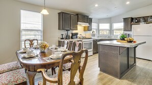A modern kitchen with dark cabinetry, a central island, and a dining area with floral-patterned chairs and a bench. - Near Ramona Wineries: Mtn-view Haven w/ Large Yard (Ramona)