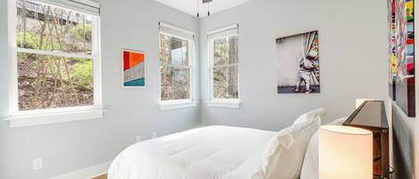 Un dormitorio con una cama, un ventilador de techo y dos ventanas con vistas a árboles.