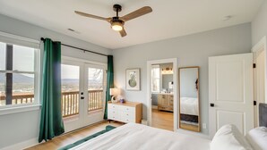 Un dormitorio con una cama grande, ventilador de techo, vista a través de una puerta corrediza, cómoda, espejo y baño visible a través de una puerta abierta.