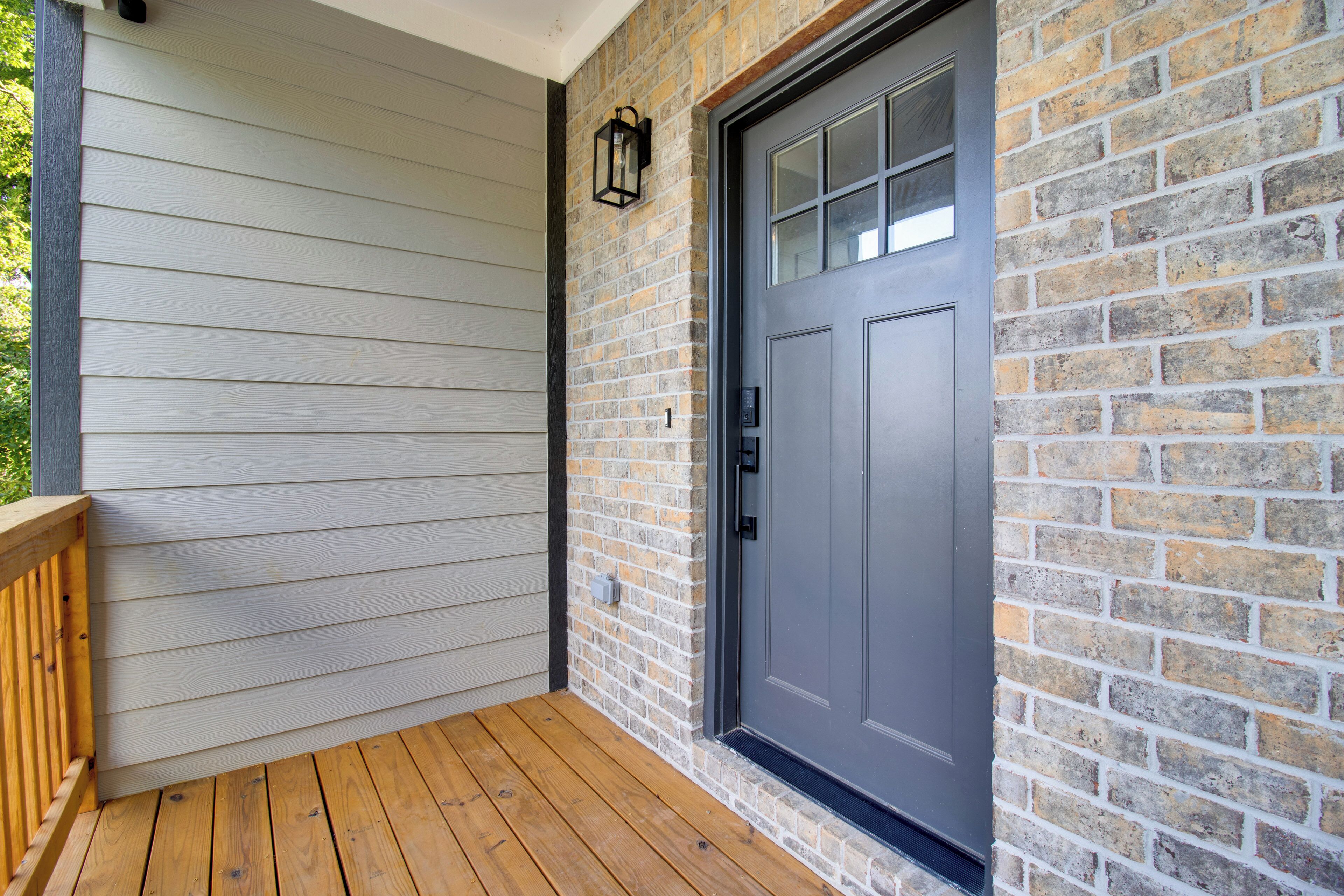 A wooden deck with a gray door and a brick wall.