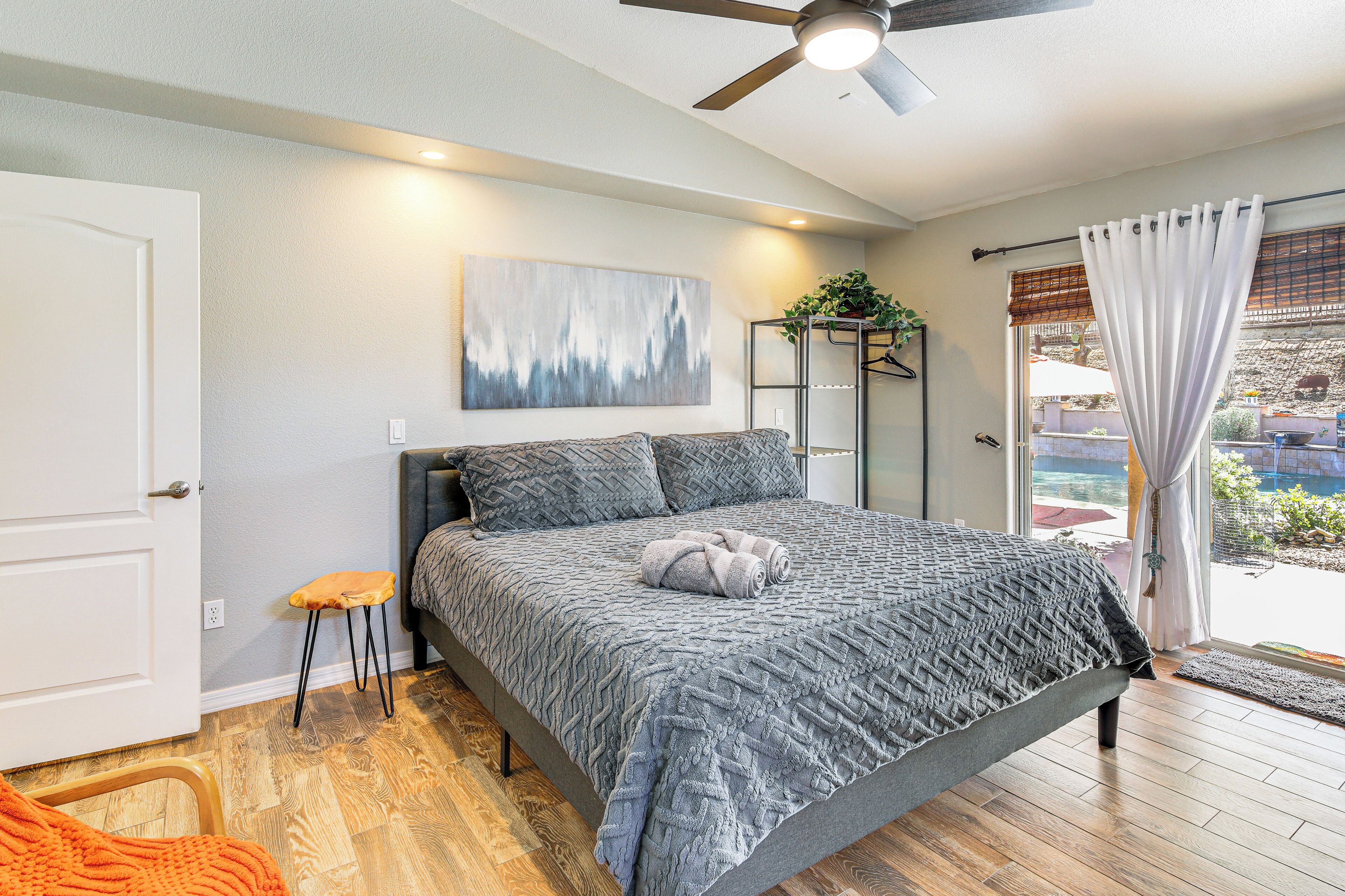 A bedroom with a bed, a ceiling fan, a window with curtains, and a door.