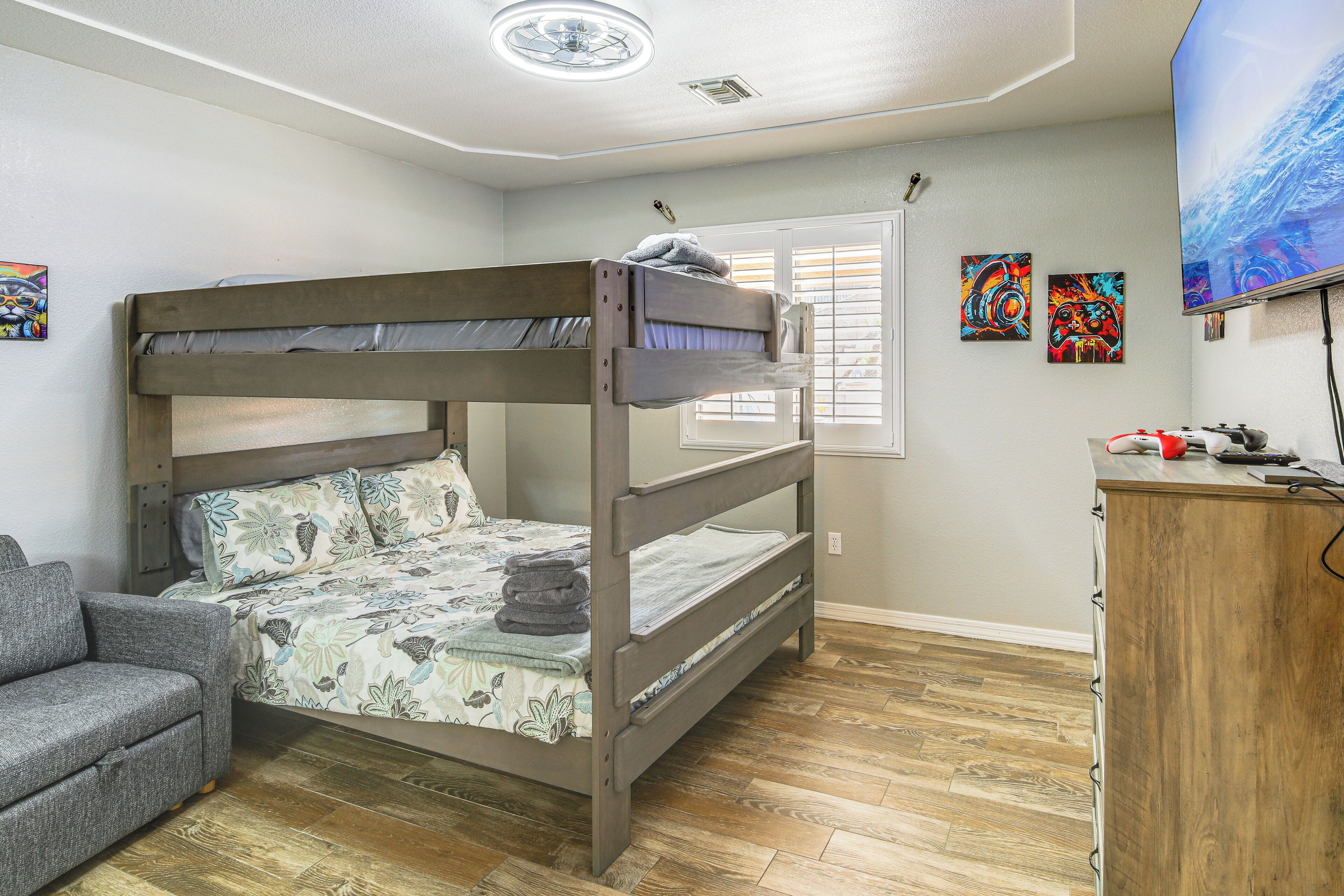A bunk bed with a grey headboard, a grey sofa, and a wooden dresser.