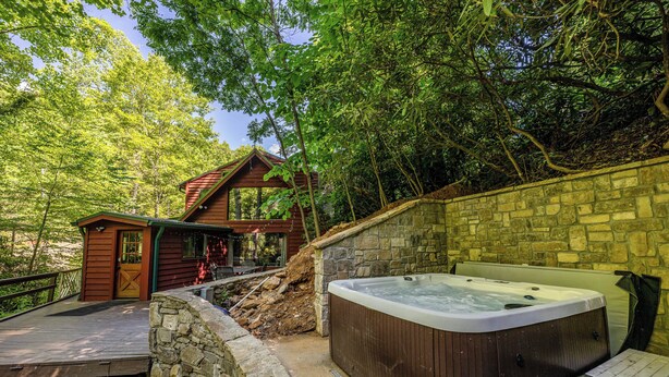 Una cabaña de madera con hidromasaje, paredes de piedra y una terraza de madera.