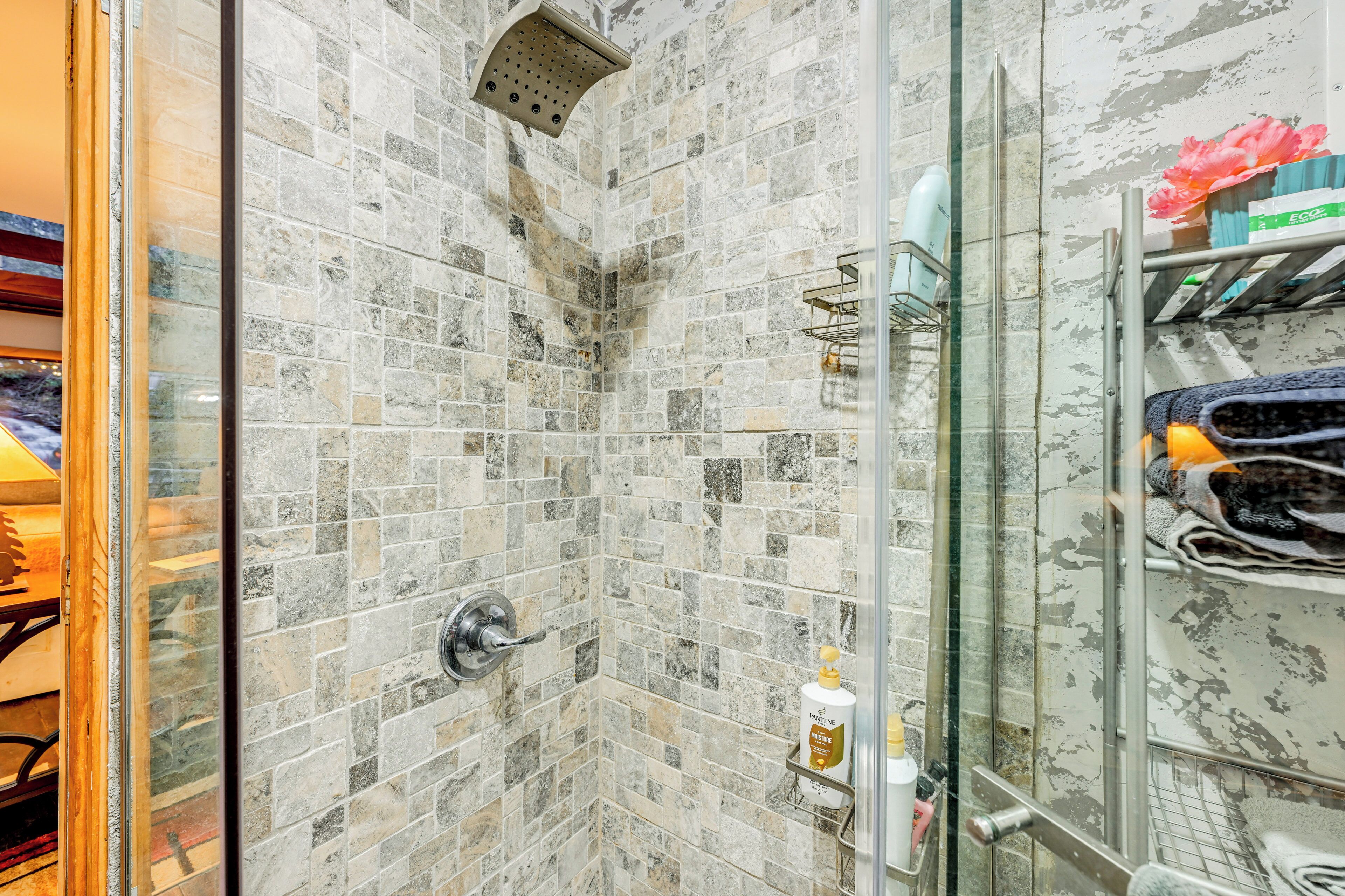 A shower area with a glass door, tiled walls, and a shelf with toiletries.
