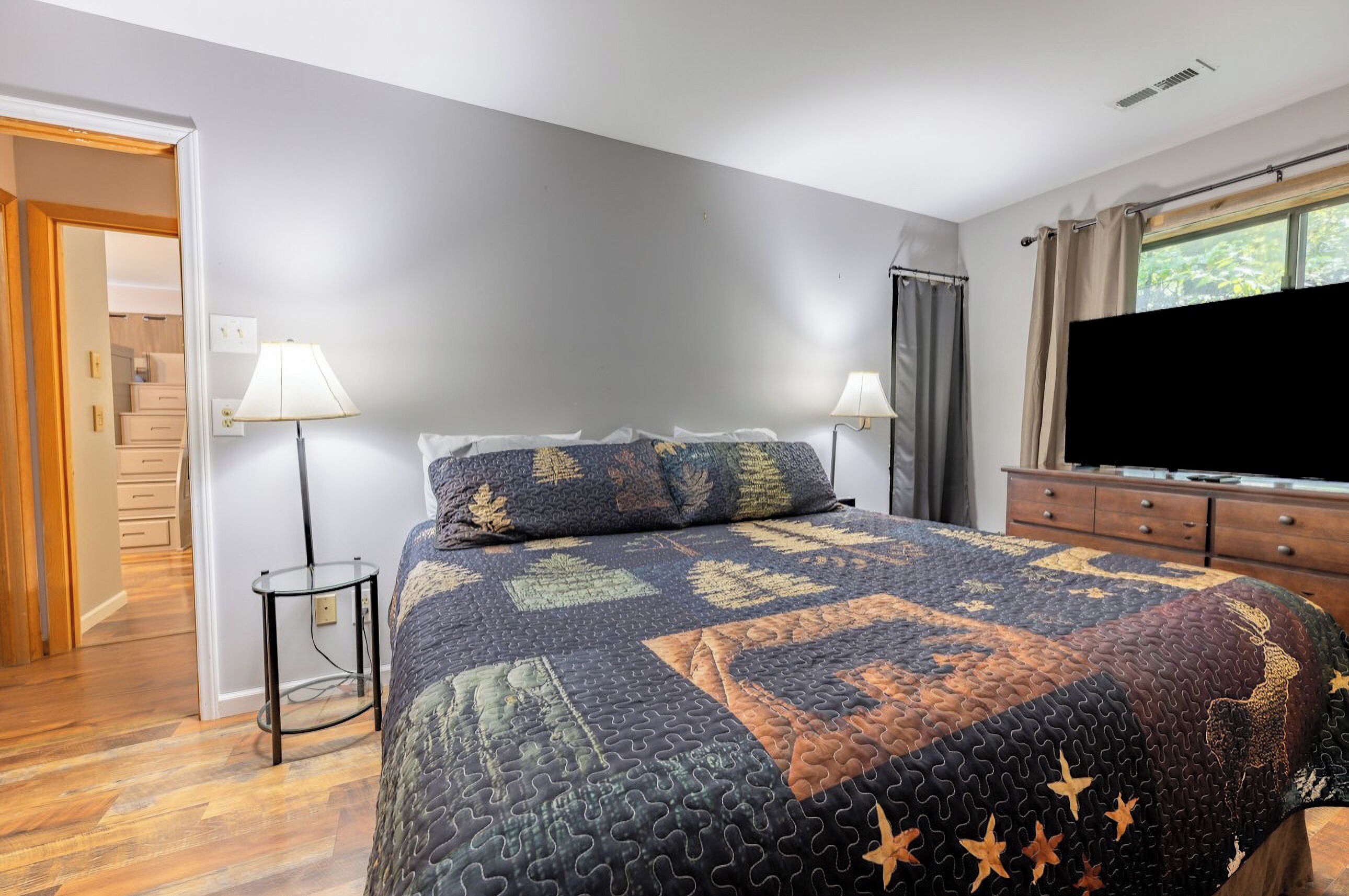 A bedroom with a large bed, two bedside lamps, a dresser, and a TV.