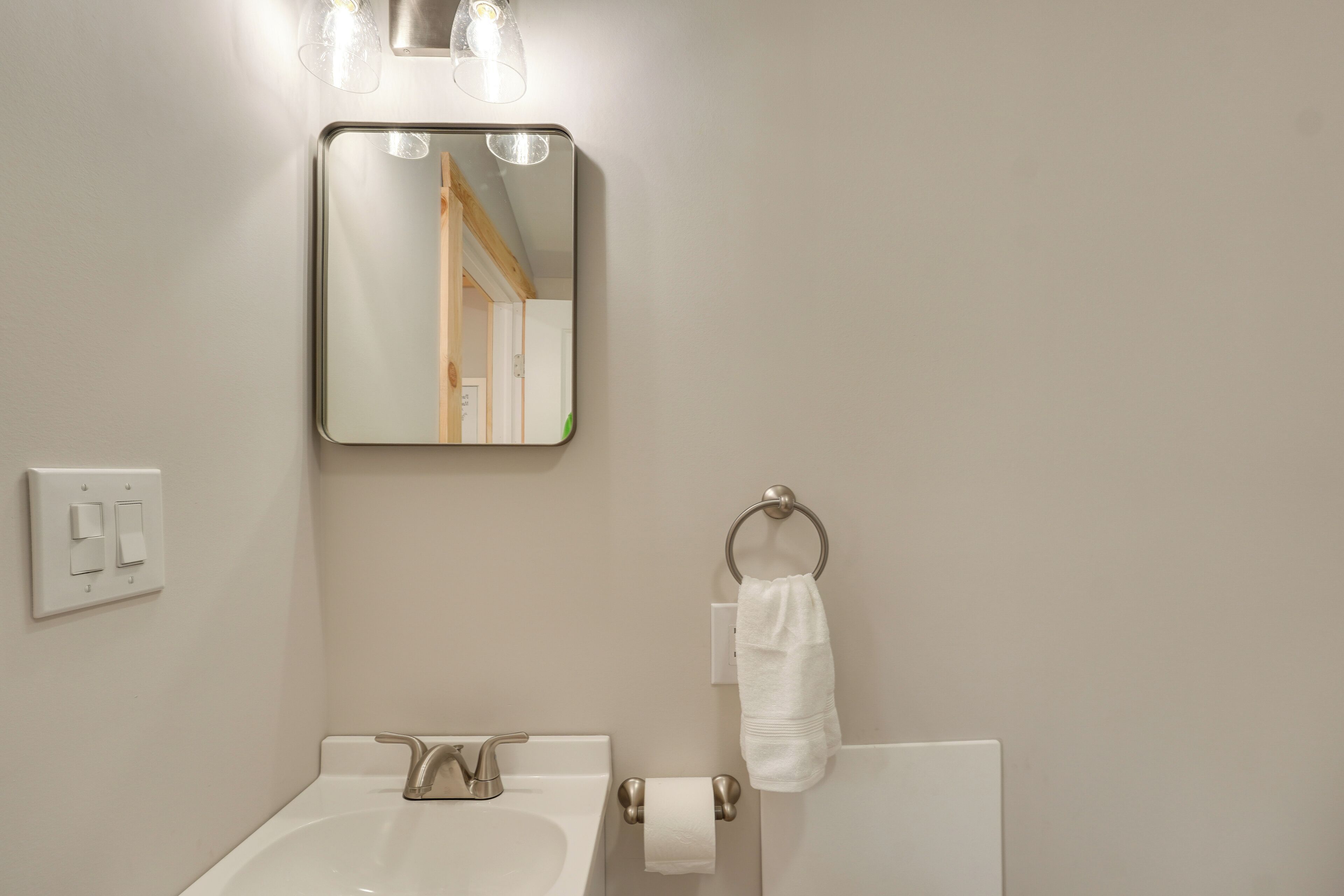 A bathroom with a sink, mirror, towel ring, and light fixture.